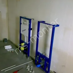 Stelaże podtynkowe Geberit zamontowane przy ścianie w surowym pomieszczeniu, widoczne elementy instalacji wodnej i kanalizacyjnej, przygotowane do zabudowy.