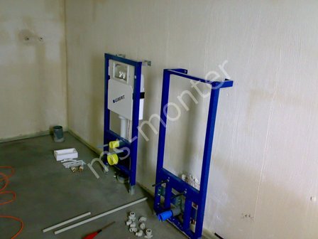 Stelaże podtynkowe Geberit zamontowane przy ścianie w surowym pomieszczeniu, widoczne elementy instalacji wodnej i kanalizacyjnej, przygotowane do zabudowy.