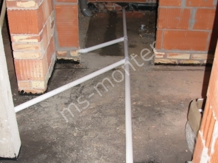 Białe rury kanalizacyjne ułożone na surowym, betonowym podłożu w trakcie montażu, widoczne ceglane ściany w tle.