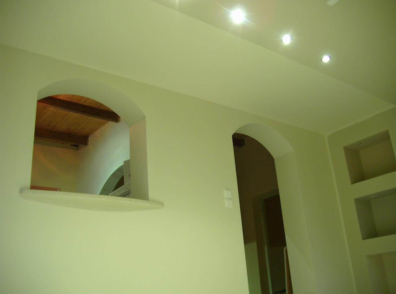 Wnętrze z łukowymi przejściami i wnękami w ścianie, wykończone w jasnej kolorystyce, z widoczną drewnianą konstrukcją stropu przez okrągłe okno.