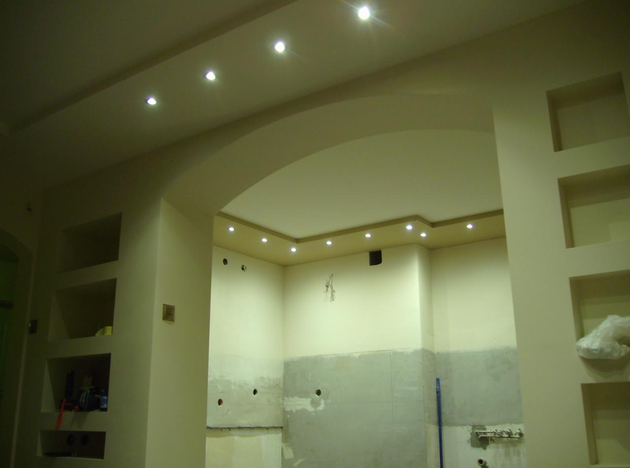 Wnętrze w trakcie remontu z widocznymi elementami zabudowy karton-gips, wnękami w ścianach i oświetleniem punktowym w suficie podwieszanym, ściany przygotowane do wykończenia.