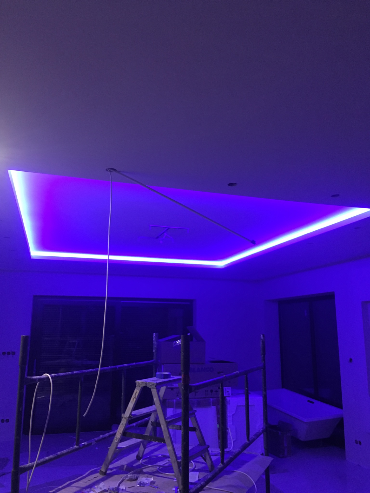 Montaż sufitu podwieszanego z oświetleniem LED RGB w pomieszczeniu w trakcie remontu, widoczne rusztowanie i przewody.