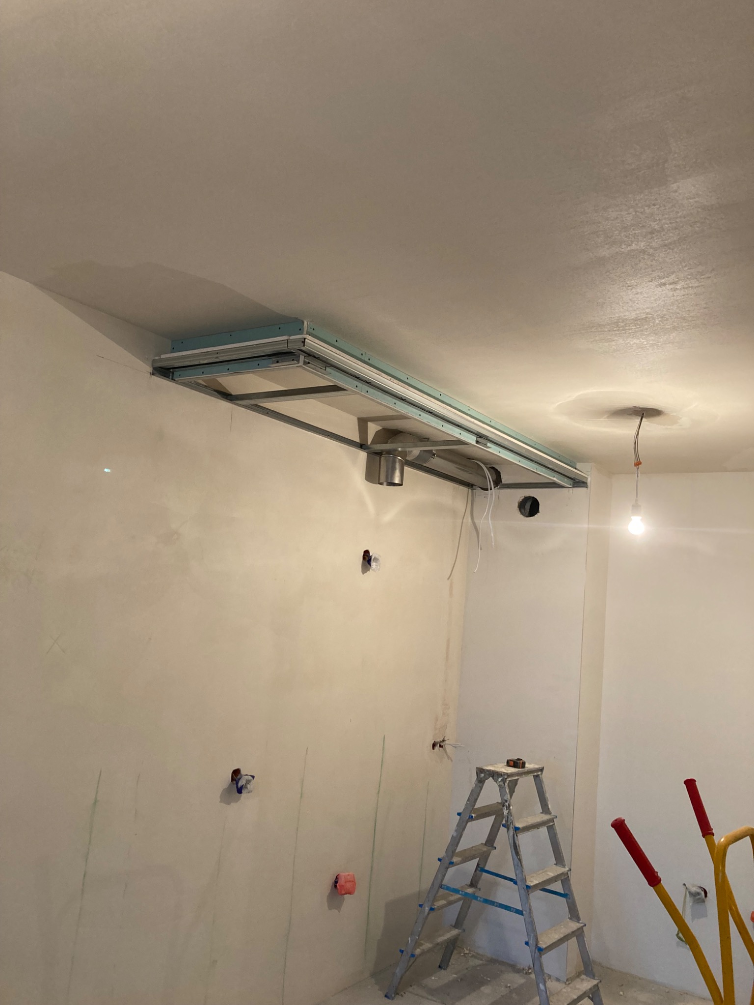 Montaż stelaża sufitu podwieszanego z widocznymi elementami instalacji wentylacyjnej, drabina aluminiowa w surowym wnętrzu z instalacją elektryczną w ścianach.