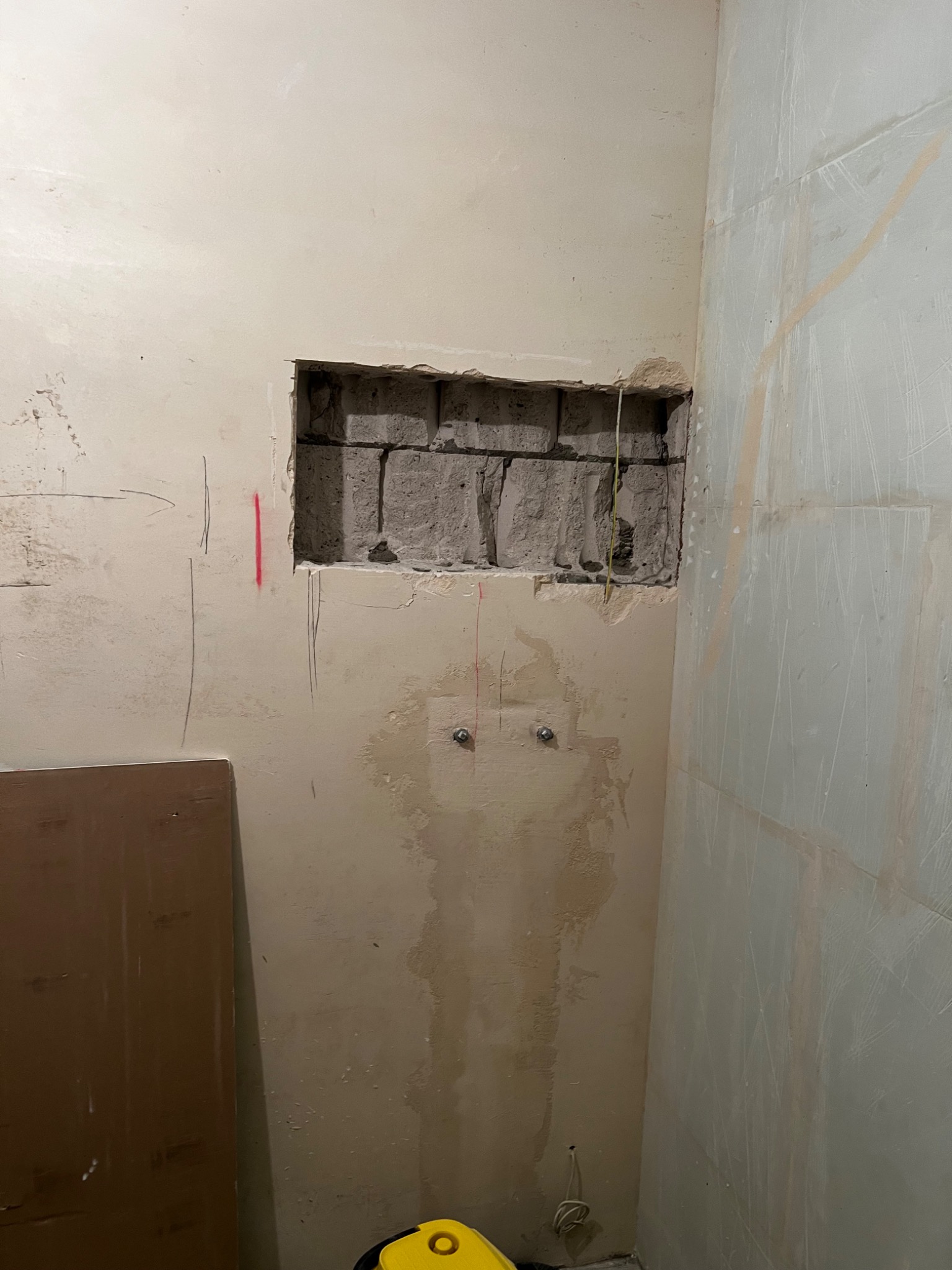 Wnęka w ścianie z widocznymi cegłami, przygotowana do dalszych prac wykończeniowych, z zaznaczonymi punktami instalacji i śladami po wcześniejszych działaniach.