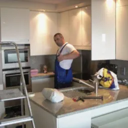 Montaż białych mebli kuchennych w Bielsku Podlaskim. Widoczny instalator w trakcie pracy oraz drabina. Nowoczesny design i oświetlenie podkreślają estetykę wnętrza.