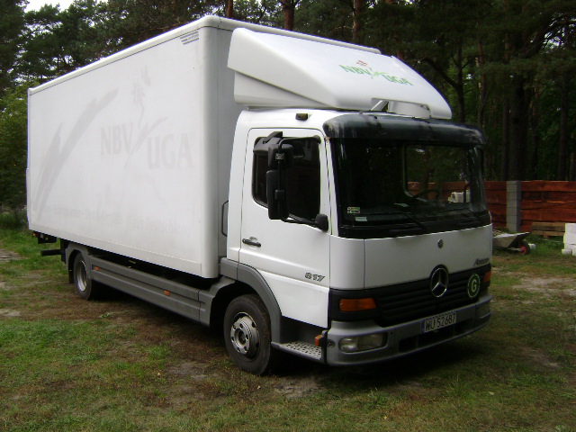 Biały samochód dostawczy Mercedes-Benz Atego 817 z nadrukiem NBV Uga na zabudowie, zaparkowany na trawie, widok z boku.
