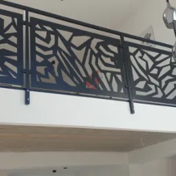 Nowoczesna balustrada wewnętrzna z czarnego metalu o geometrycznym wzorze, zamontowana na antresoli z widocznym betonowym stropem i wiszącymi lampami w tle.