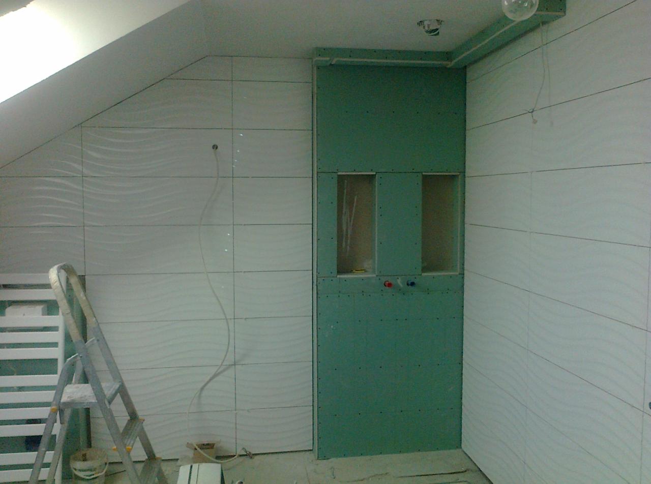 Montaż płytek z falistym wzorem na ścianach poddasza w trakcie prac, widoczna drabina, fragment ściany z płyt gipsowo-kartonowych z otworami na instalacje.