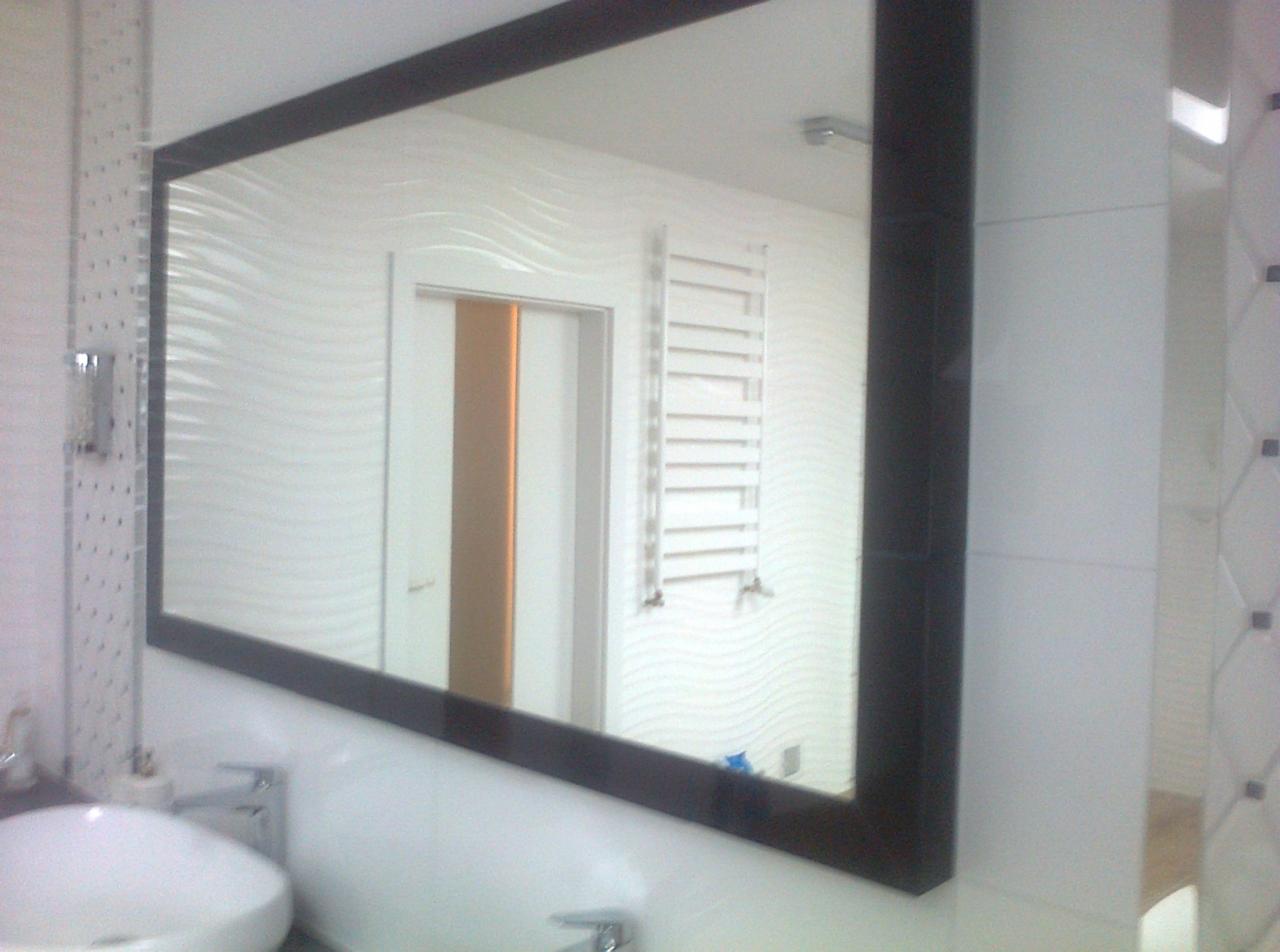 Nowoczesna łazienka z dużym lustrem w ciemnej ramie, odbijającym falistą strukturę białych płytek ściennych i grzejnik drabinkowy