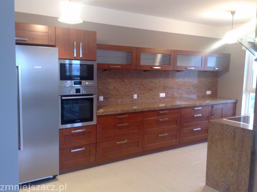 Kuchnia na wymiar z drewnianymi frontami, blatem z brązowego marmuru, srebrną lodówką Bosch i wbudowanym piekarnikiem oraz mikrofalówką.