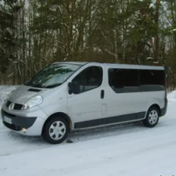 Srebrny bus Renault Trafic z ciemnymi szybami, zaparkowany na śniegu w zimowej scenerii leśnej.