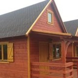 Firma Handlowa MS - Rząd trzech identycznych, drewnianych domków letniskowych z brązowymi dachami i okiennicami, widocznych z perspektywy lekko z boku. Domki mają małe zadaszone werandy z drewnianymi balustradami.