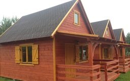 Rząd trzech identycznych, drewnianych domków letniskowych z brązowymi dachami i okiennicami, widocznych z perspektywy lekko z boku. Domki mają małe zadaszone werandy z drewnianymi balustradami.