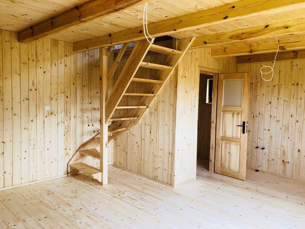 Wnętrze wykończone drewnem: podłoga, ściany i sufit z boazerii, drewniane schody spiralne prowadzące na górę oraz drewniane drzwi z przeszkleniem.