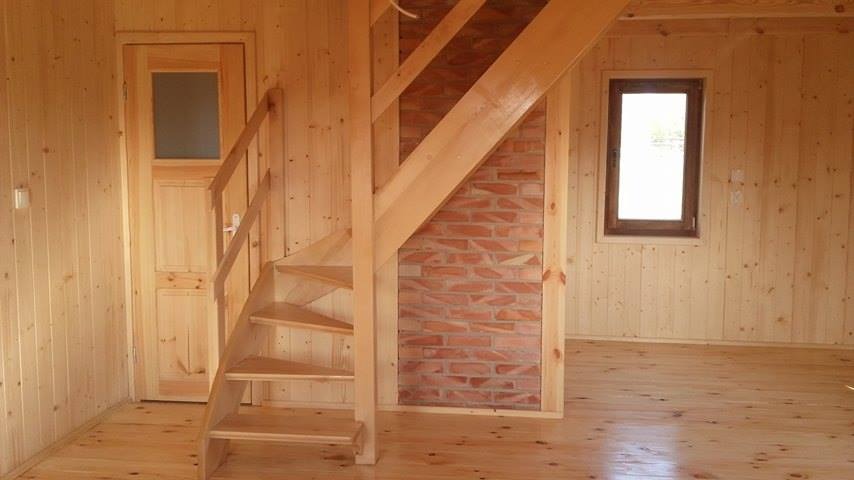 Wnętrze domu wykończone drewnianą boazerią z drewnianymi schodami i fragmentem ściany z cegły.