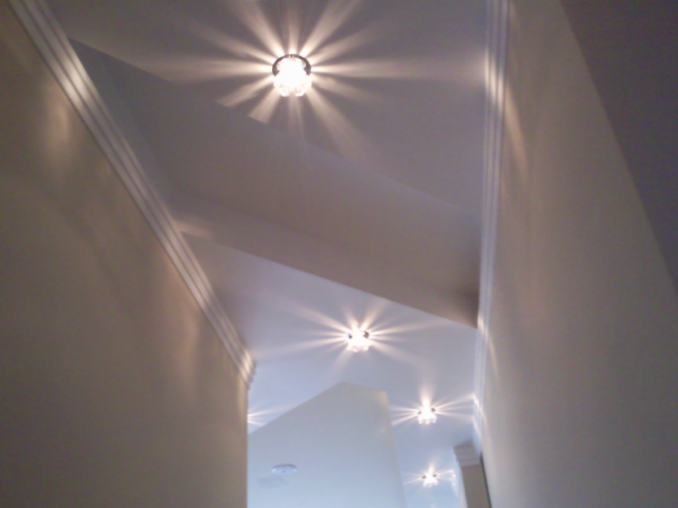 Wnętrze korytarza z trzema lampami sufitowymi oświetlającymi białe ściany i sufit.