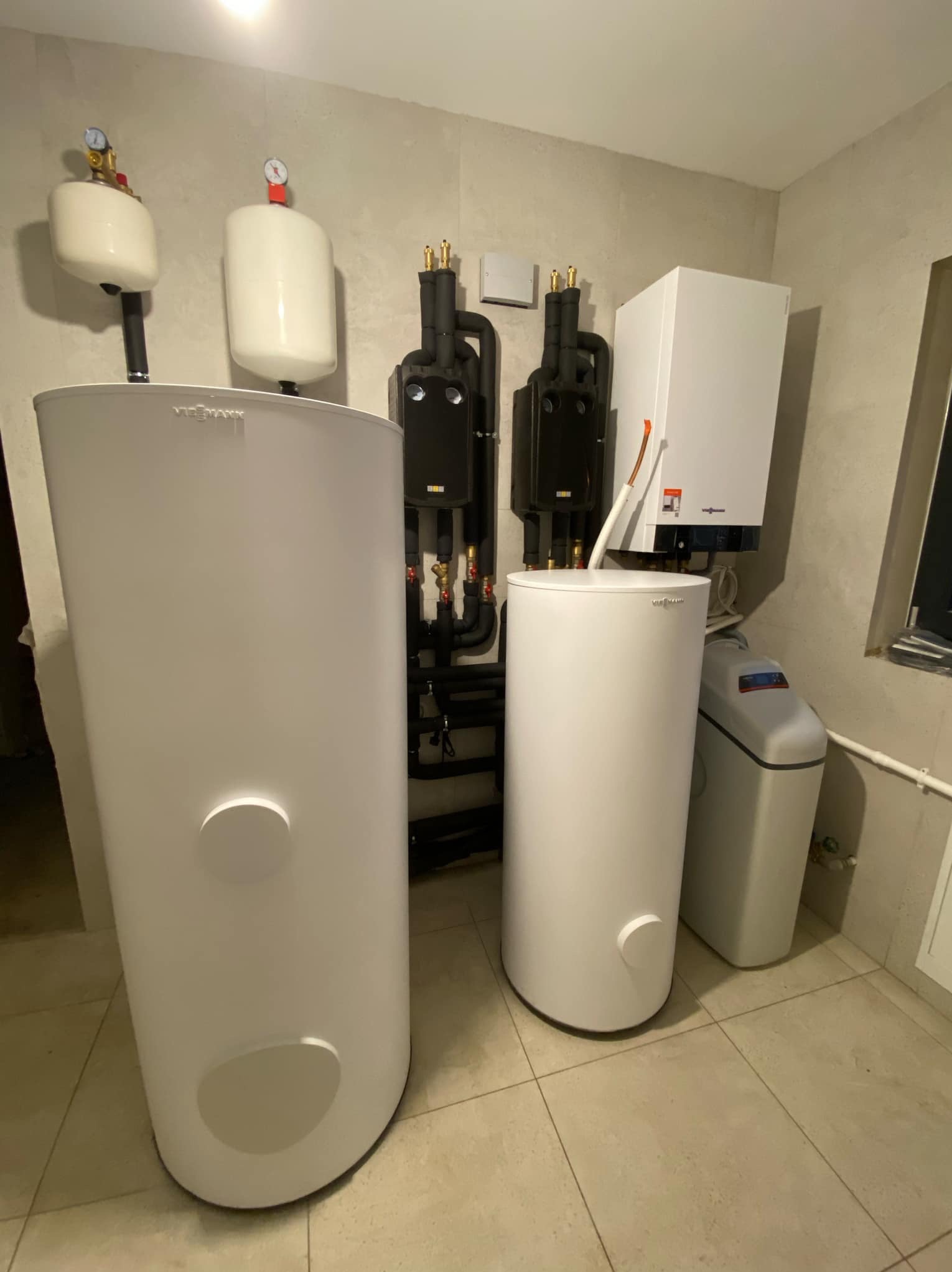 Zestaw urządzeń grzewczych Viessmann: pompa ciepła typu split, zasobnik c.w.u. 300L, bufor 200L, dwie grupy pompowe z zaworem mieszającym oraz zmiękczacz wody, zainstalowane w kotłowni z szarymi...