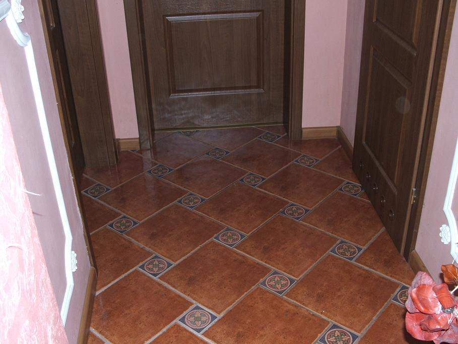 Ukończona podłoga w łazience wyłożona brązowymi płytkami z dekoracyjnymi wstawkami, widoczne dwie drewniane futryny drzwiowe i fragment ściany w odcieniach różu.