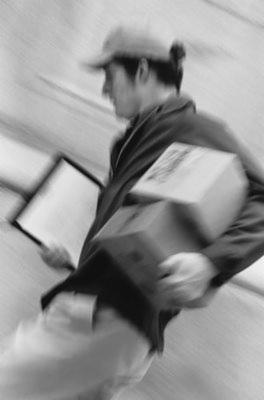 Rozmazane, czarno-białe zdjęcie kuriera w biegu z paczką i dokumentami, dynamiczne ujęcie.