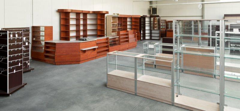 Wnętrze magazynu w Koszalinie z ekspozycją różnorodnych regałów magazynowych, w tym drewnianych lad i przeszklonych gablot, gotowych do zagospodarowania towarem.