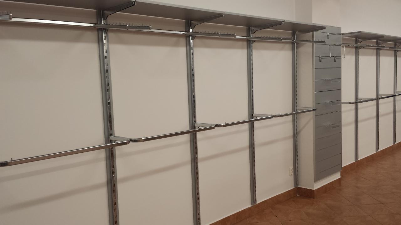 Metalowe, modułowe systemy regałowe zamontowane na ścianie, z poziomymi drążkami i półkami, tworzące przestrzeń do ekspozycji towarów w sklepie.