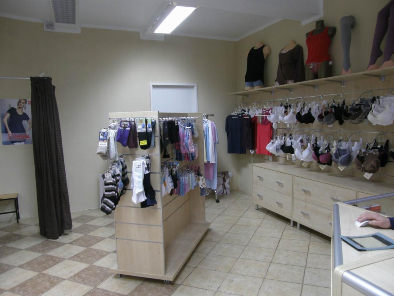 Wnętrze sklepu z bielizną, regały z skarpetami i rajstopami, manekiny prezentujące odzież, ekspozycja biustonoszy na ścianie, jasne meble i kafelkowana podłoga.