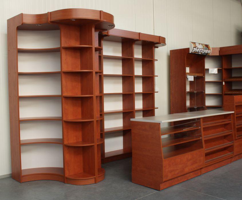 Wysokie, drewniane regały sklepowe z półkami o różnej głębokości, w tym półki o zaokrąglonym kształcie, ustawione w sklepie z szarym betonowym podłożem.