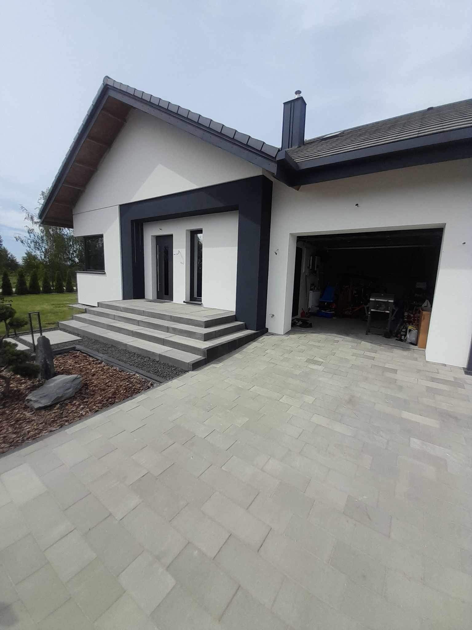 Nowoczesny dom jednorodzinny w Sulęcinie z wykończoną elewacją w kolorach bieli i grafitu, widoczne schody wejściowe wyłożone kamieniem oraz podjazd z kostki brukowej.