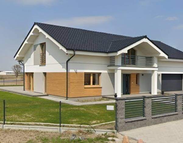 Nowoczesny dom jednorodzinny z elewacją w kolorze białym i elementami drewnianymi, czarny dach z dachówki, balkon z metalową balustradą i szara brama garażowa.