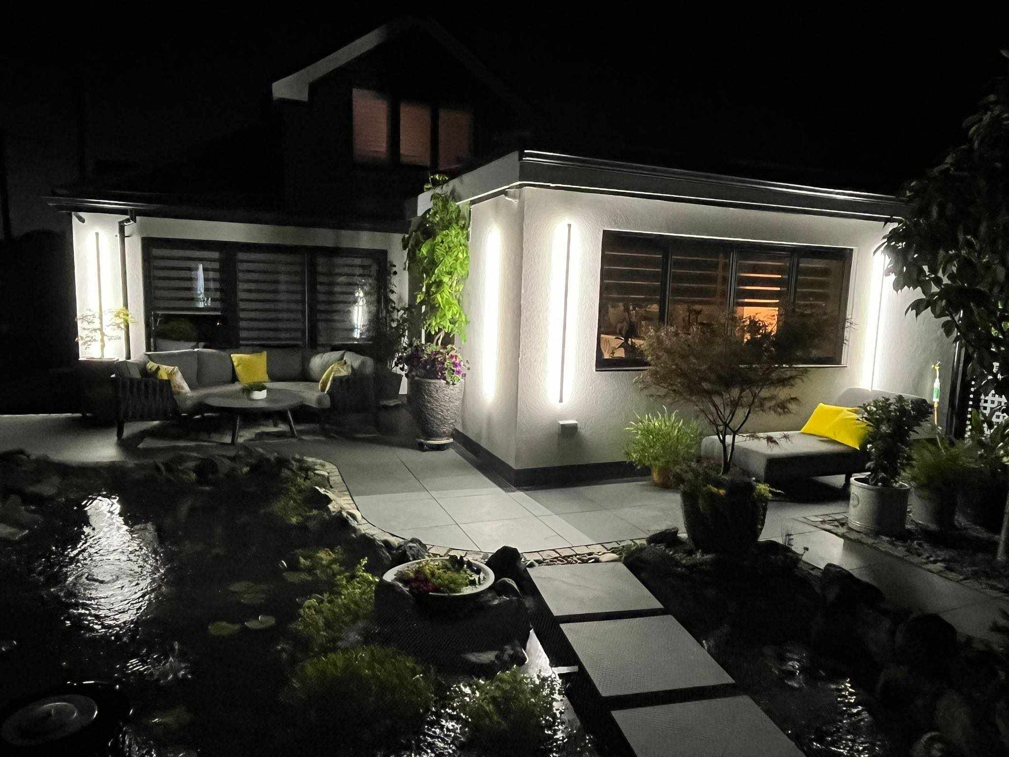 Nowoczesny dom z oświetloną elewacją i tarasem z oczkiem wodnym, widok nocny.