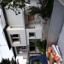 Dwupiętrowy dom jednorodzinny w trakcie odnawiania elewacji, widok z wnętrza skrzyni ładunkowej samochodu dostawczego, z workami zaprawy murarskiej Kreisel na pierwszym planie.