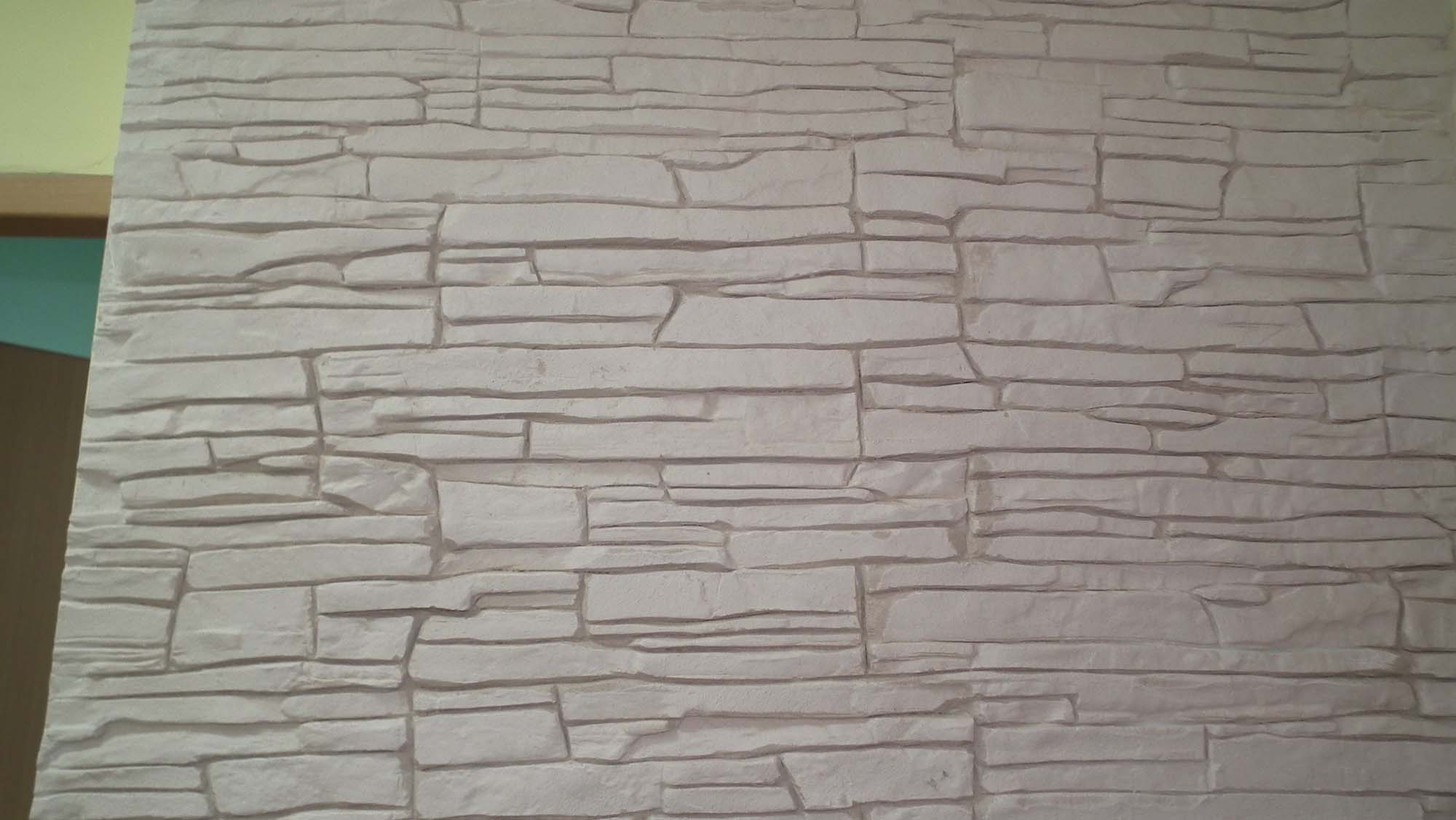 Ściana wyłożona dekoracyjnym piaskowcem w odcieniach bieli i szarości, z widocznym fragmentem pomalowanej ściany w tle.