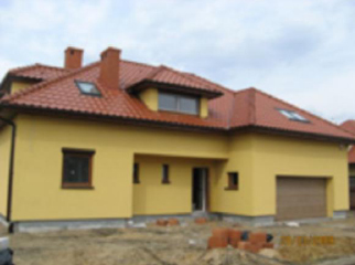 Żółty dom jednorodzinny z czerwoną dachówką, widok z zewnątrz, częściowo rozmazany obraz.