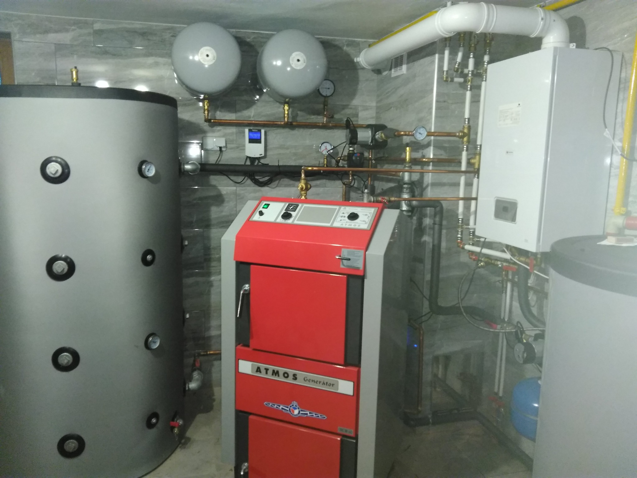 Kotłownia z czerwonym piecem na paliwo stałe Atmos Generator, zbiornikiem akumulacyjnym i instalacją z rur miedzianych.