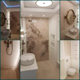 Elegancka łazienka w odcieniach beżu i bieli z armaturą w kolorze starego złota, marmurowe płytki na ścianie prysznica, owalna umywalka na białym blacie, dekoracyjne lustro w złotej ramie, biała...