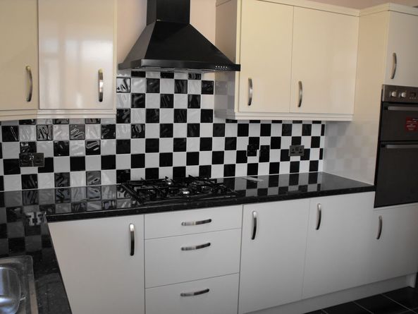 Wykończona kuchnia z białymi szafkami, czarnym blatem, płytą gazową i czarno-białą mozaiką na ścianie.