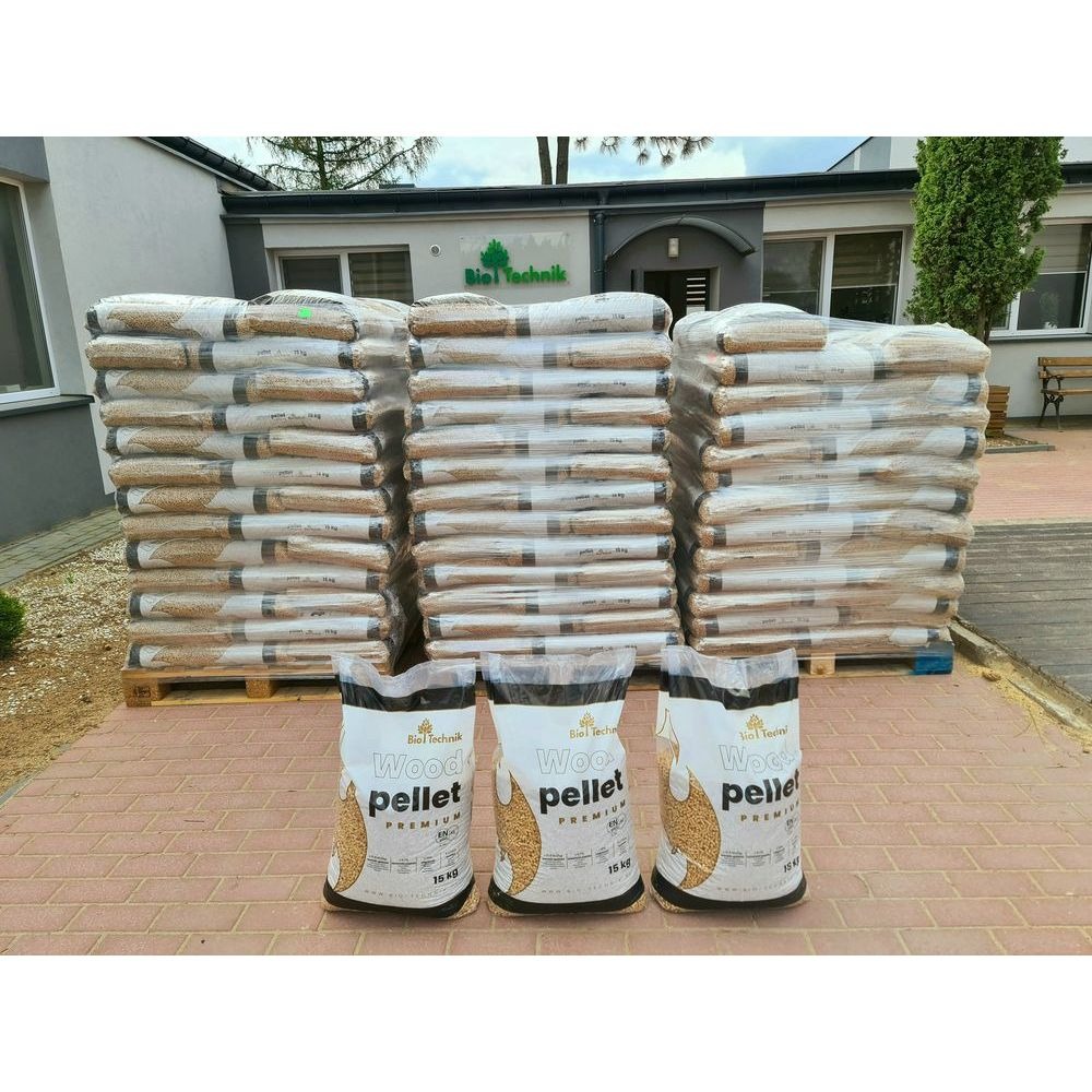 Stosy worków z pelletem drzewnym na paletach przed budynkiem firmy Bio Technik, z trzema workami 15kg na pierwszym planie.