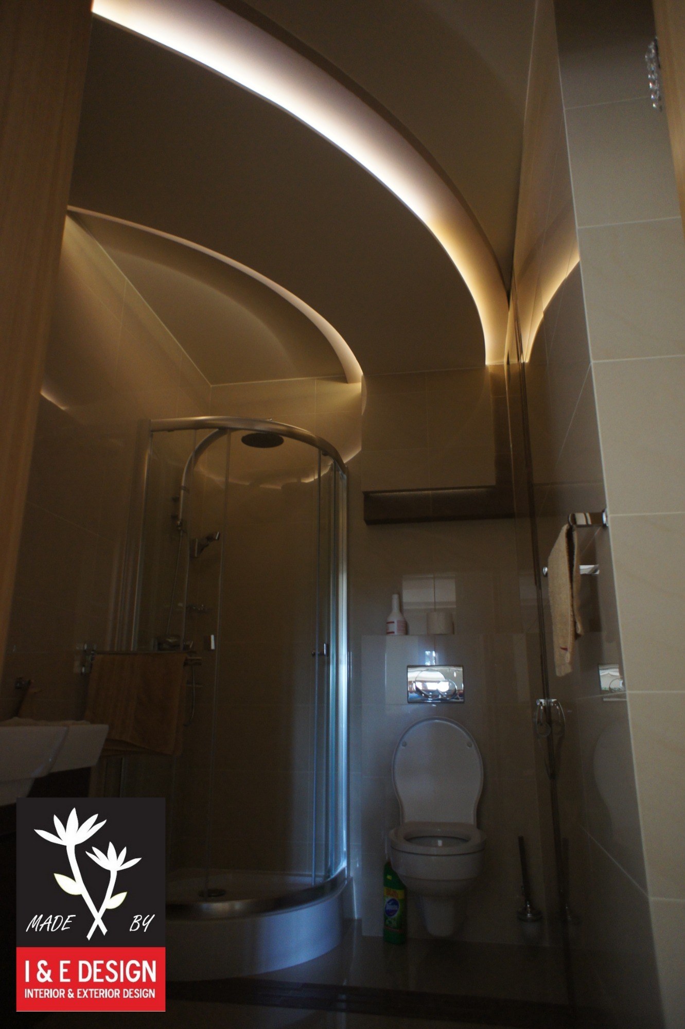 Nowoczesna łazienka z kabiną prysznicową, podwieszanym sufitem z oświetleniem LED i beżowymi płytkami ceramicznymi na ścianach.