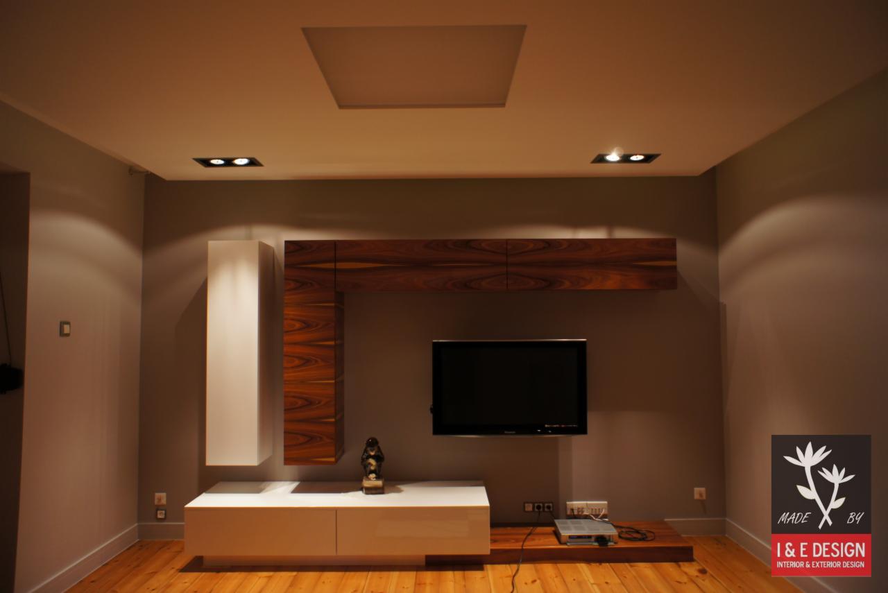 Nowoczesny salon z drewnianą podłogą i meblami na ścianie w odcieniach bieli i brązu. Podwieszany sufit z oświetleniem punktowym.