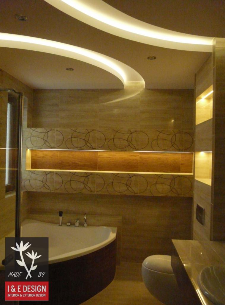 Nowoczesna łazienka z podświetlanym sufitem i geometrycznym wzorem na płytkach. Uwagę przykuwa wanna narożna i staranne wykończenie.