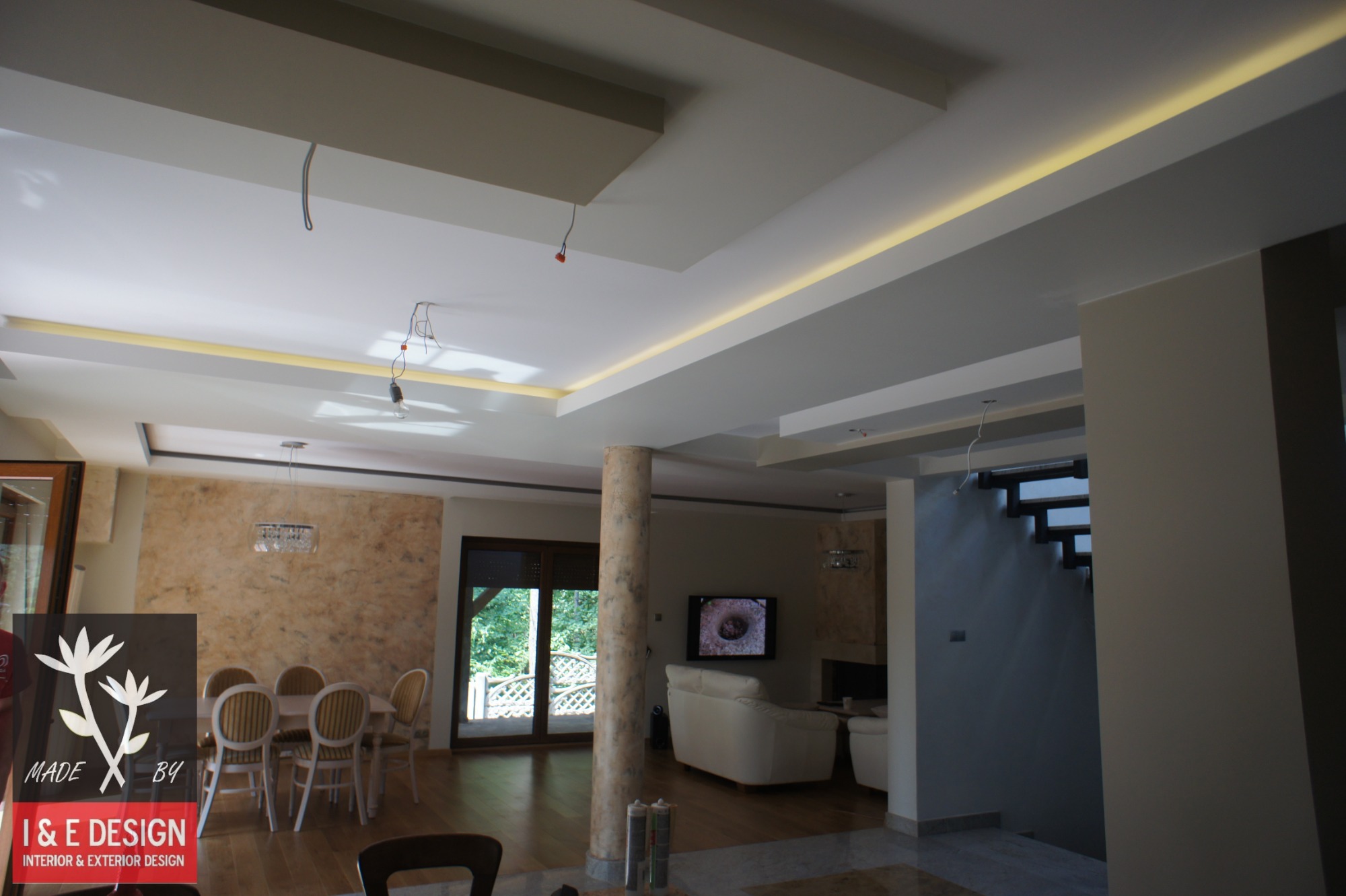 Wnętrze domu z widocznym sufitem podwieszanym z oświetleniem LED, kolumną dekoracyjną, jadalnią i salonem z kominkiem oraz schodami.