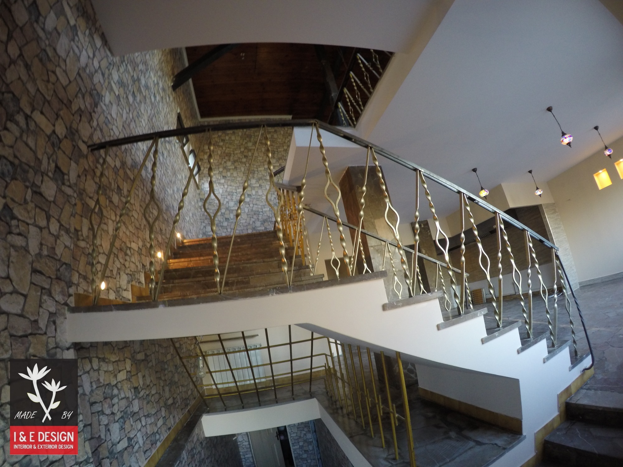 Wnętrze z kamienną ścianą i schodami z metalową balustradą o dekoracyjnym wzorze.