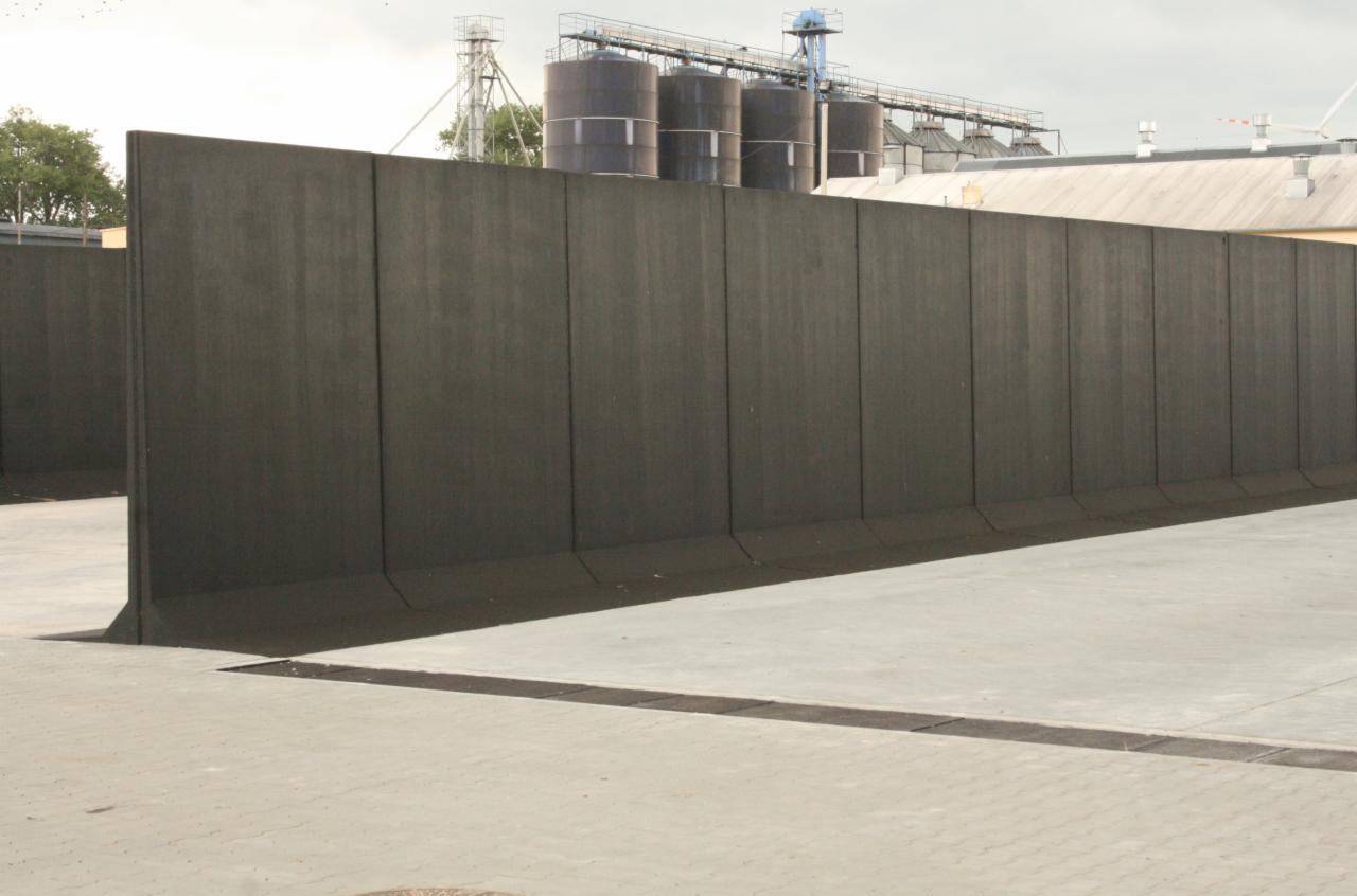 Prefabrykowane betonowe ściany oporowe na placu budowy, z silosami zbożowymi w tle.