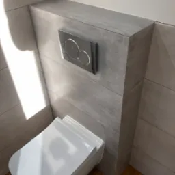 Podwieszana toaleta z szarymi płytkami imitującymi beton, chromowany przycisk spłukujący, drewnopodobna podłoga i cień na ścianie.