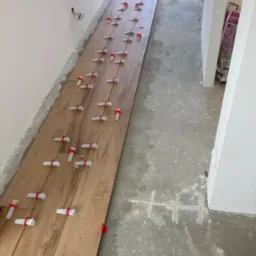 Układanie podłogi z płytek imitujących drewno z użyciem klipsów poziomujących, widoczne ślady po zaprawie na podłożu.