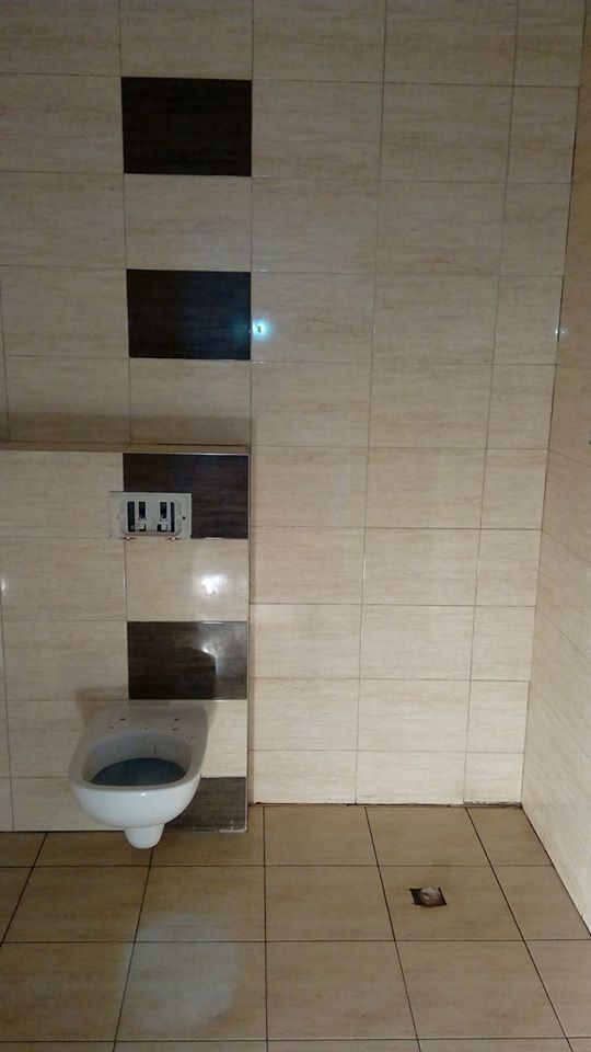 Wykończona łazienka z beżowymi i brązowymi płytkami. Wisząca toaleta z widocznym stelażem. Na podłodze płytki w odcieniach beżu. Widoczny odpływ liniowy.