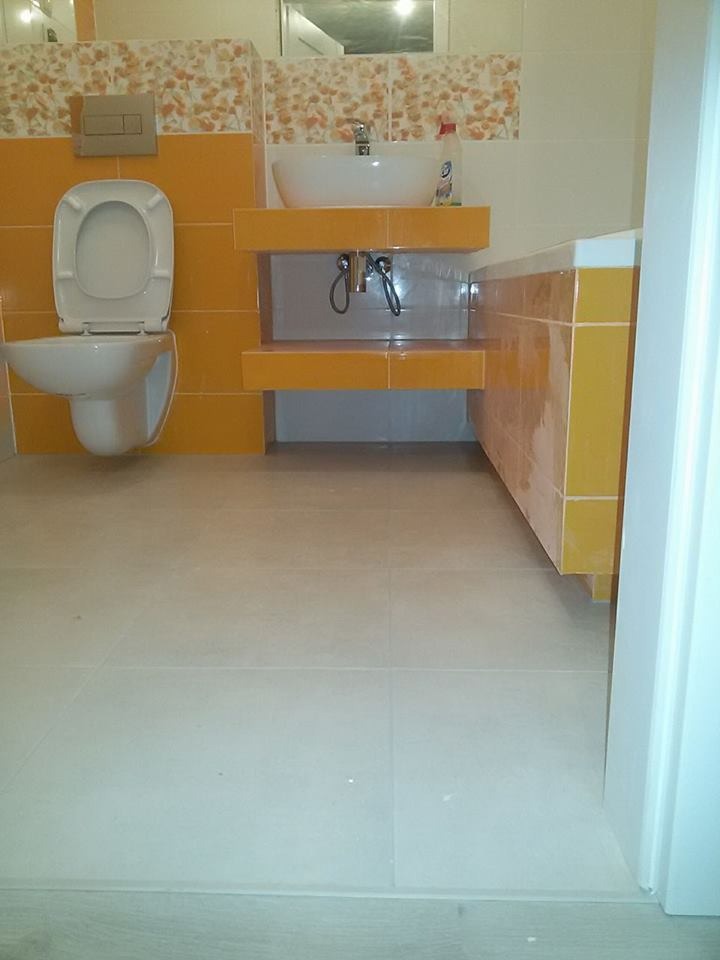 Żółto-biała łazienka po remoncie: toaleta, umywalka na podwieszanej szafce, płytki z motywem kwiatowym. Widok z poziomu podłogi, świeżo po ukończeniu prac.