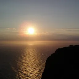 Zachód słońca nad morzem, widok z klifu z sylwetkami ludzi i globusem na tle nieba w ciepłych barwach.