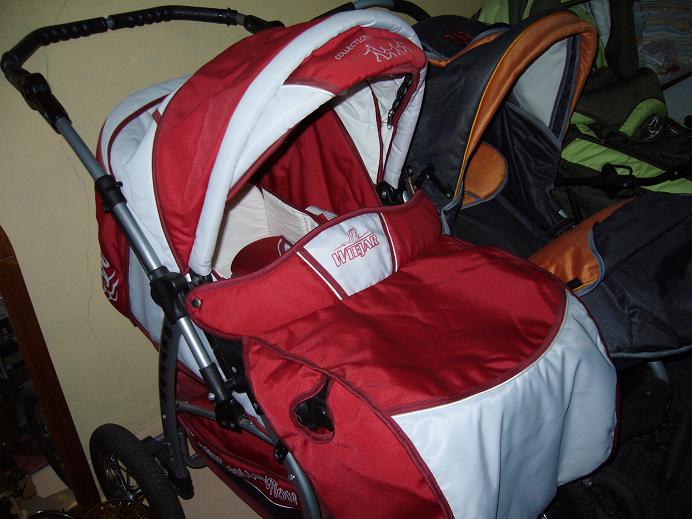 Czerwono-biały wózek wielofunkcyjny dziecięcy z aluminiowym stelażem i czarnymi kołami, widoczne inne wózki w tle.