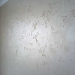 Ściana wewnętrzna z dekoracyjną, beżowo-złotą fakturą, widoczna z boku, z fragmentem białej firany po lewej stronie.